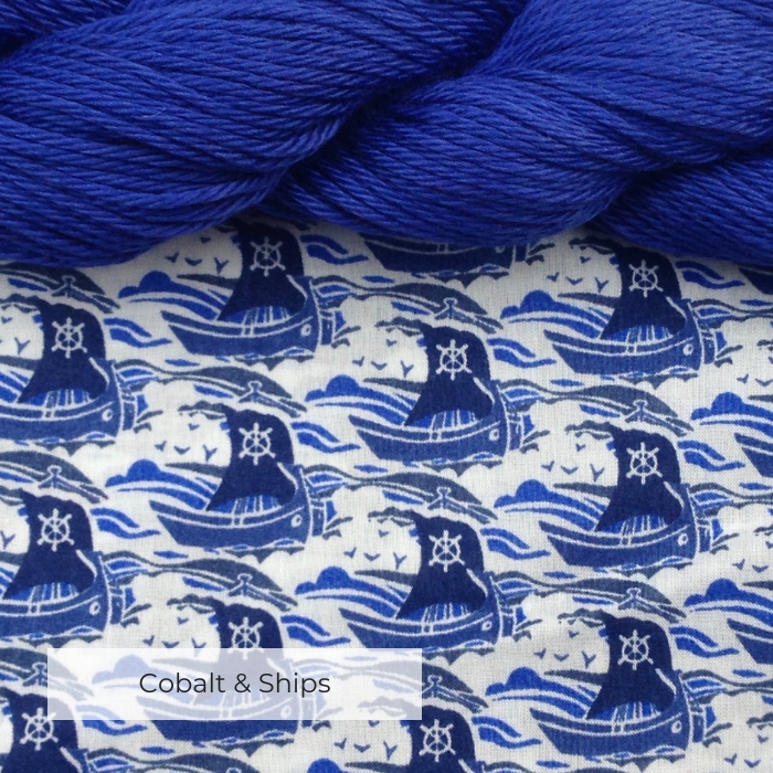 Bright cobalt blue cotton yarn at the top of a piece of fabric printed with blue sailing boats