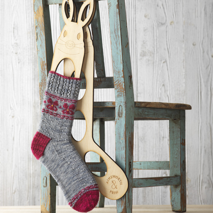 Grey and red hand knit sock with Fair Isle pattern blocked on rabbit shaped shock blockers hanging on the back of a chair