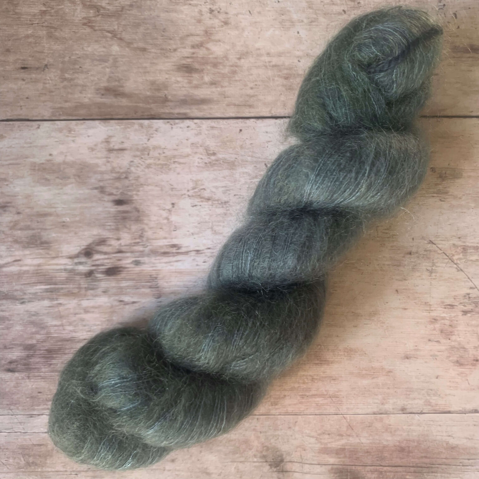 One skein blue, grey mohair silk yarn on pale wood background.