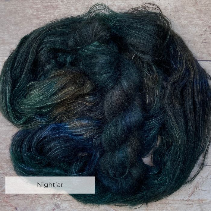 Two skeins of very dark blue variegated mohair and silk lace weight yarn on pale wood background