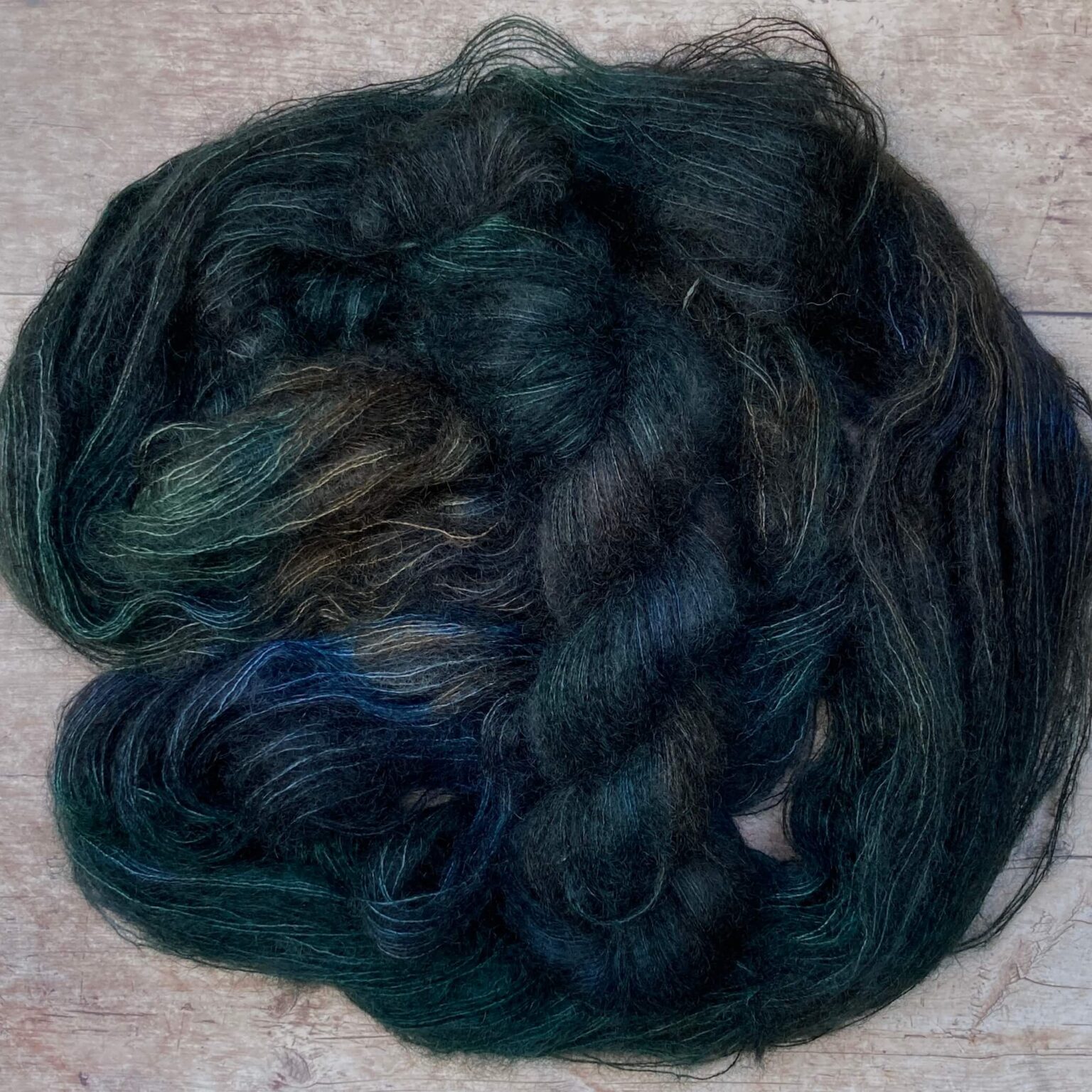 Two skeins of very dark blue variegated mohair and silk lace weight yarn on pale wood background