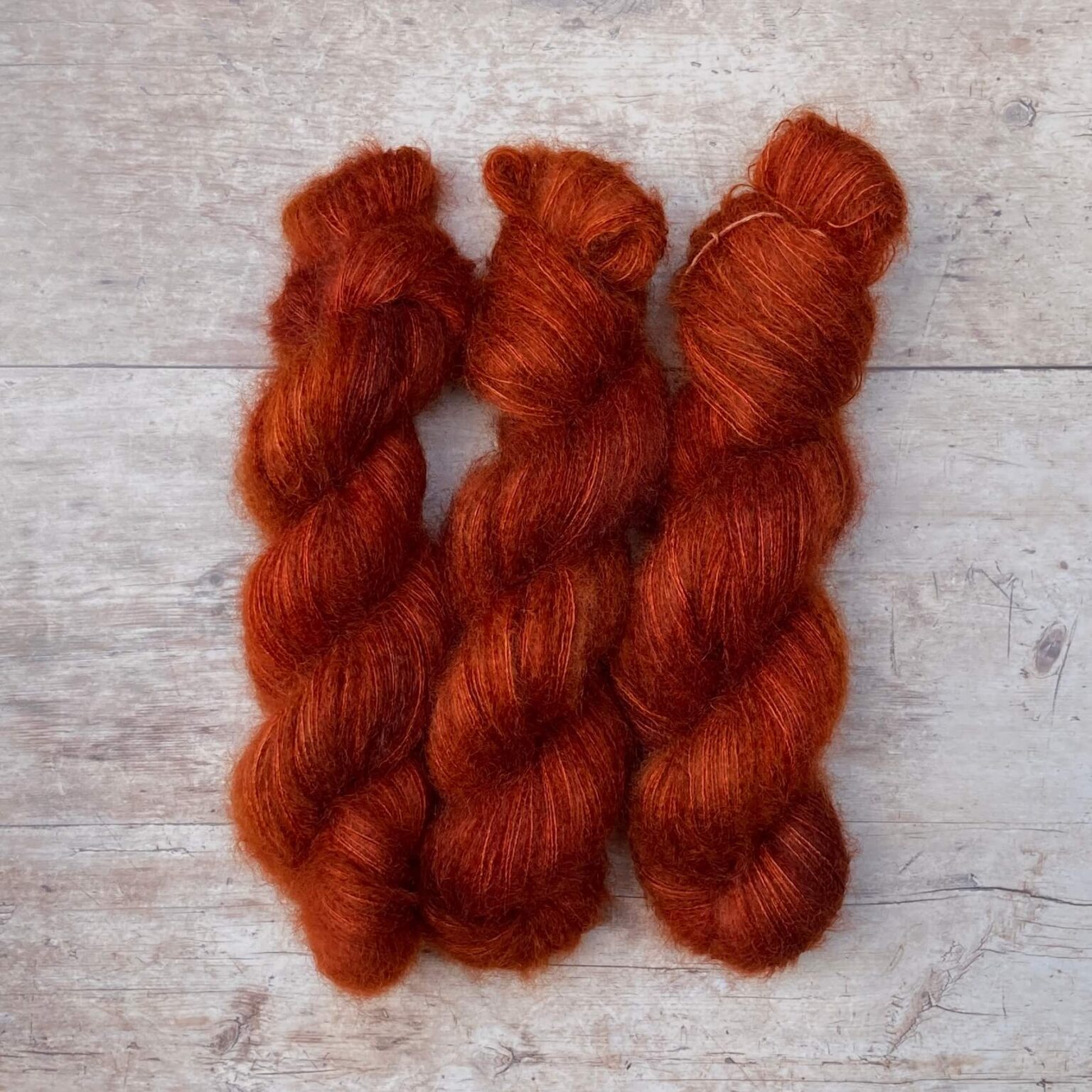 Three skeins of rusty orange mohair and silk lace yarn on pale wood background