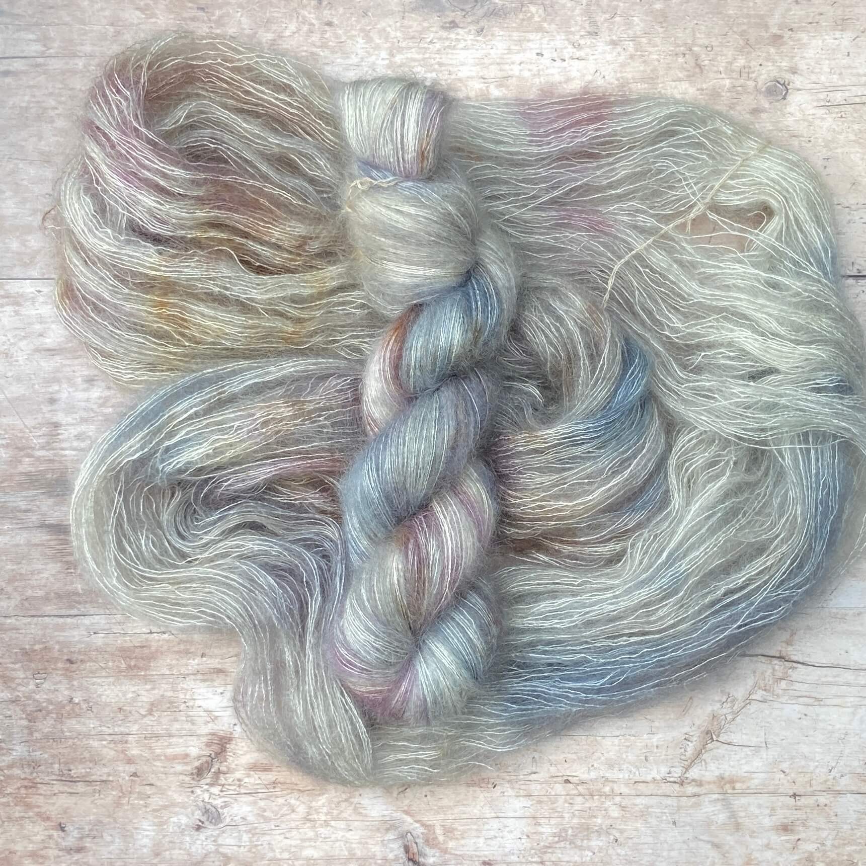 Two skeins Mohair Silk lace weight yarn in soft warm grey, speckled with brown on pale wood surface