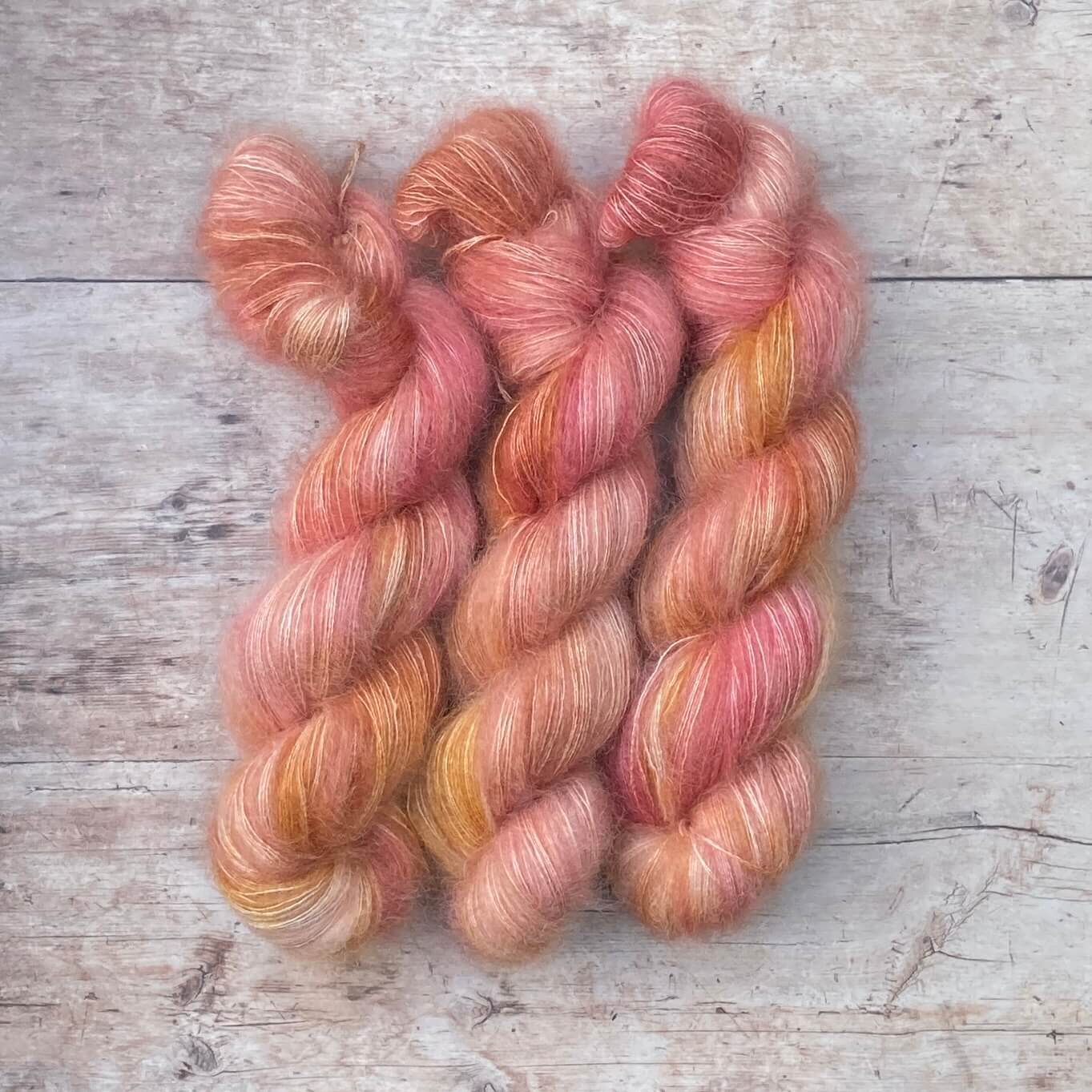 Three skeins of Pink and coral variegated mohair and silk lace yarn on pale wood background