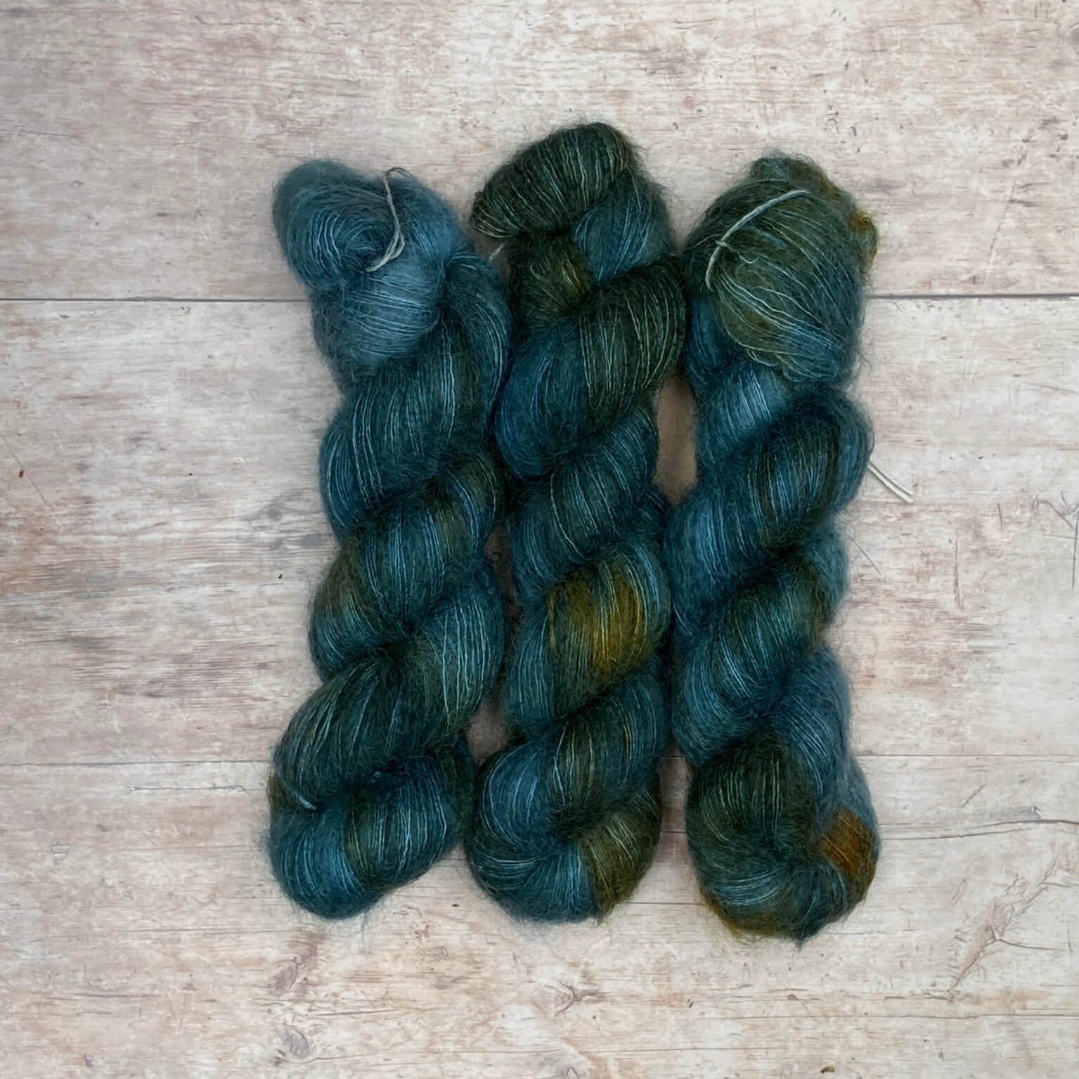 three skeins of mohair and silk lace in blue and dark teal yarn splashed with marmalade orange