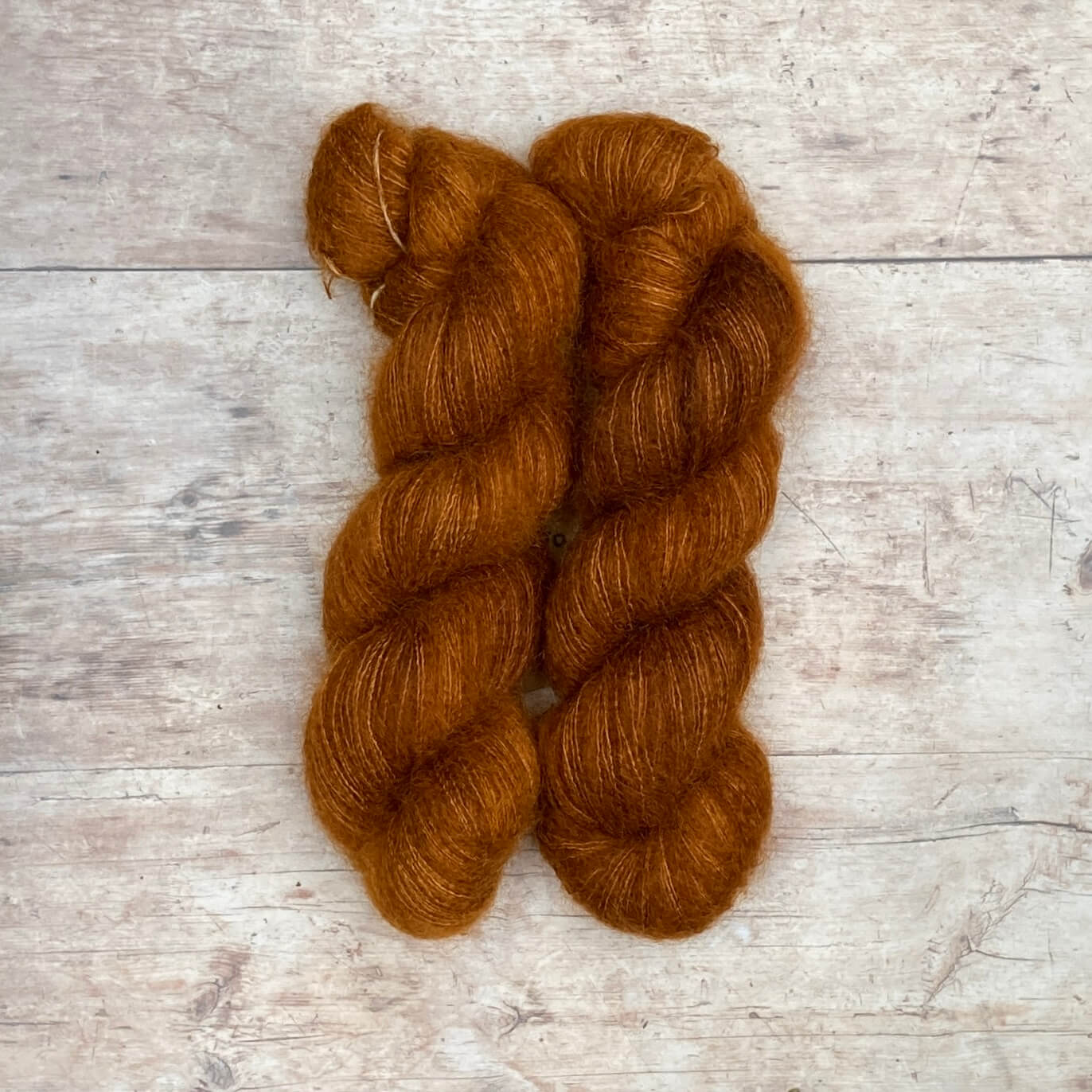 Two skeins of rusty brown mohair and silk lace yarn on pale wood background