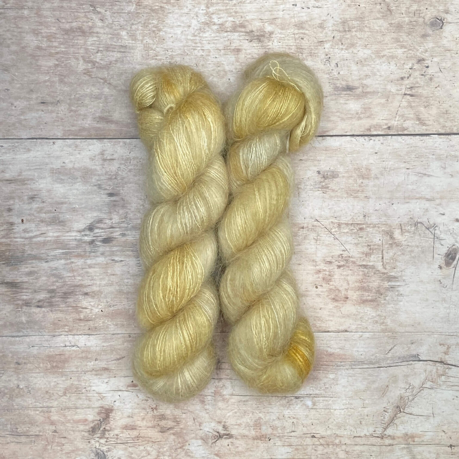 Two skeins of cream and yellow mohair and silk lace yarn on pale wood background