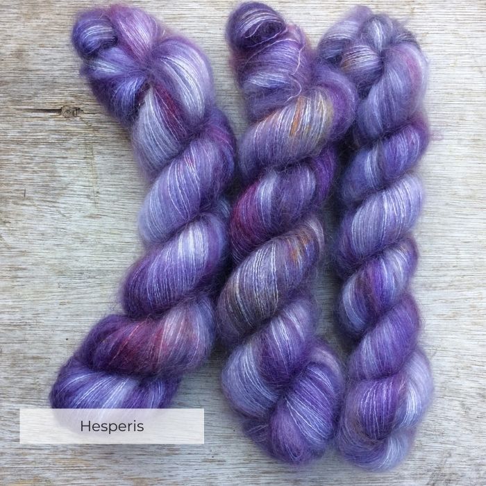 Three skeins of yarn dyed in shades of violet, grey and purple with splashes of pink and yellow