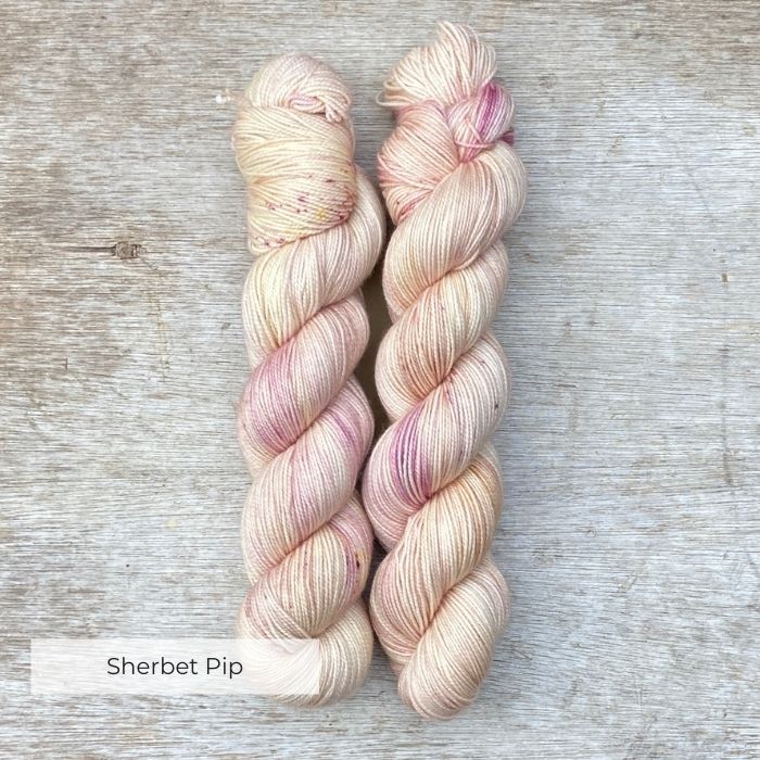Two skeins of pale pink and cream yarn lightly speckled with plums and golds