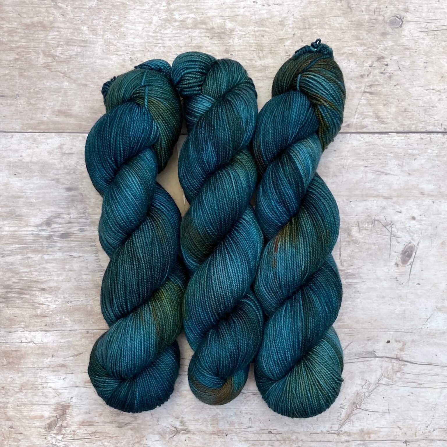 Three skeins classic sock in mid to dark blue with orange variegation on pale wood surface