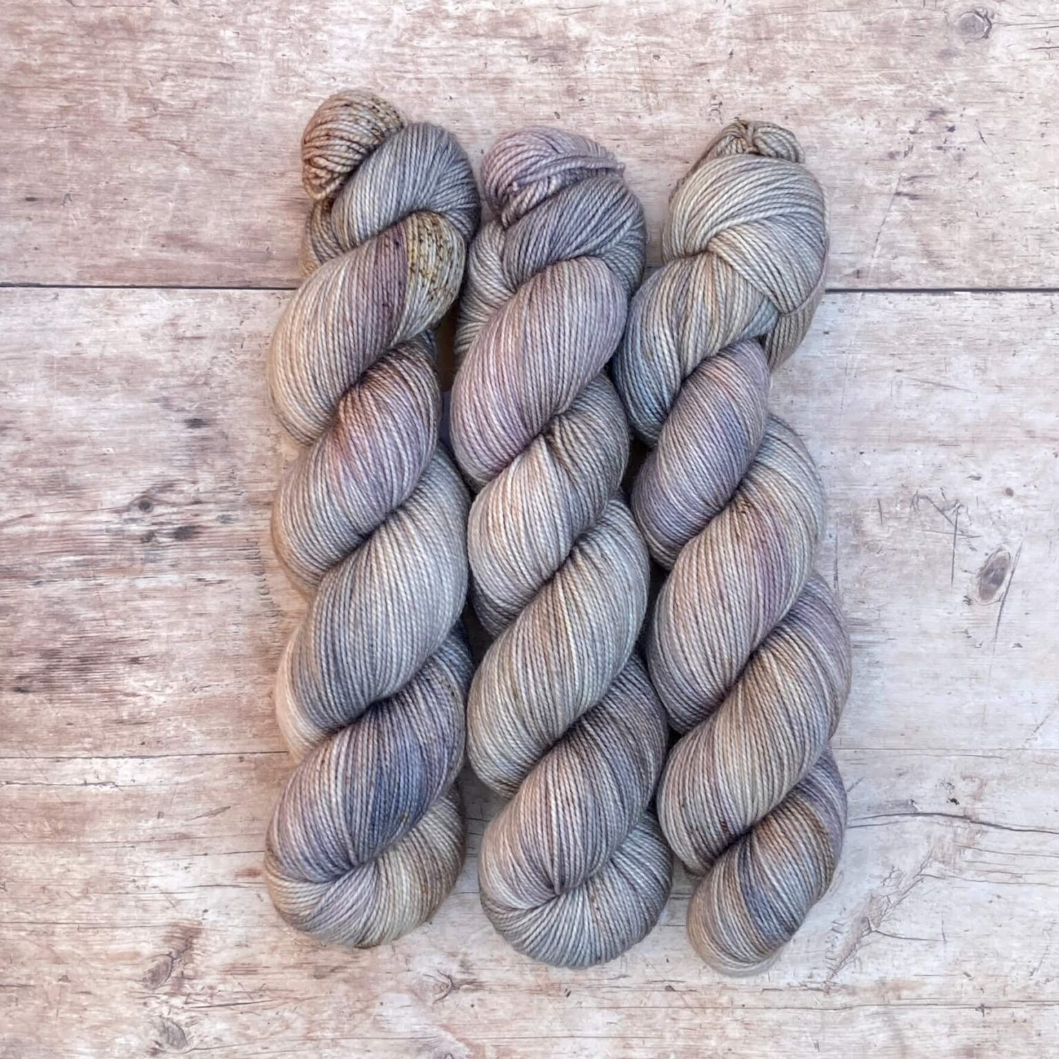 Three skeins classic sock in soft warm grey, speckled with brown on pale wood surface