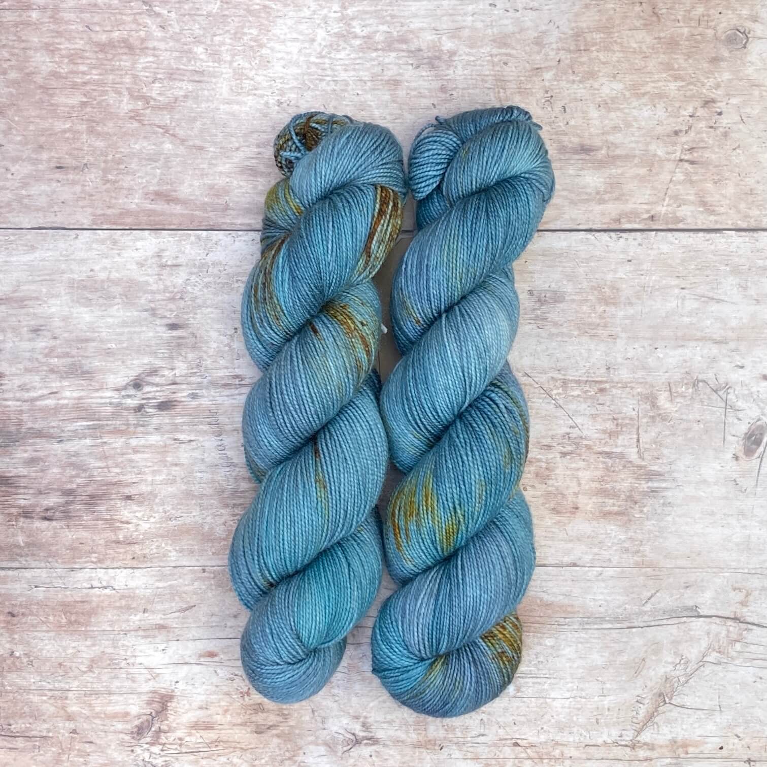 Two skeins classic sock in mid blue and teal with tan speckles on pale wood surface