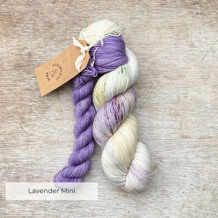 A multicoloured skein of sock yarn in green, lilac and lavender with a lavender mini skein.