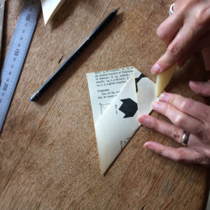 Pair of hands using a bone folder to fold an envelope on a wooden table