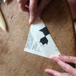 A pair of hands folding a paper square in to an envelope on a wooden table