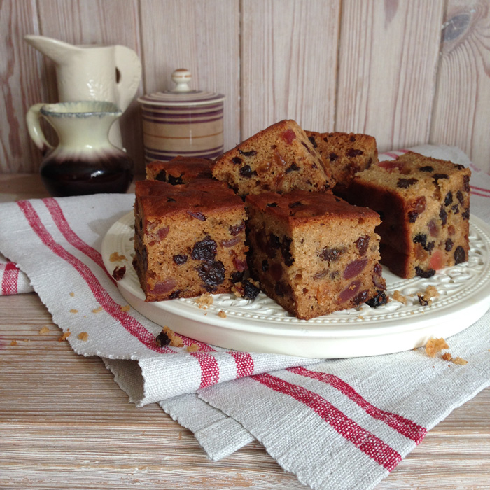 A cream plate with large slices of fruitcake on a folded linen cloth and against a wooden background