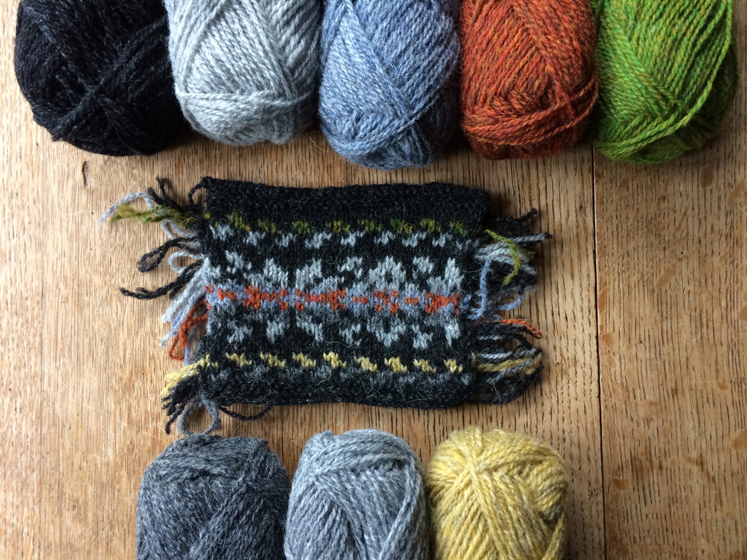 A swatch of knitted colour work with the responding coloured wool above them
