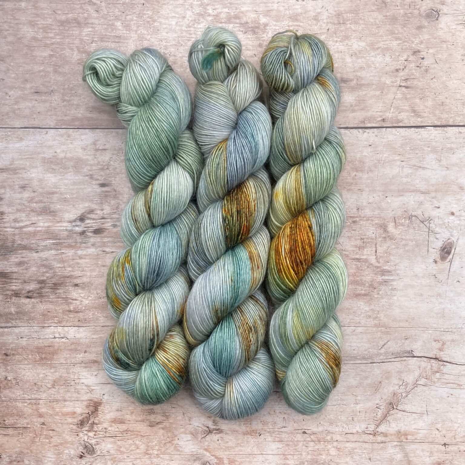 Three skeins of Merino Floof in shades of light blue and green with gold splashes