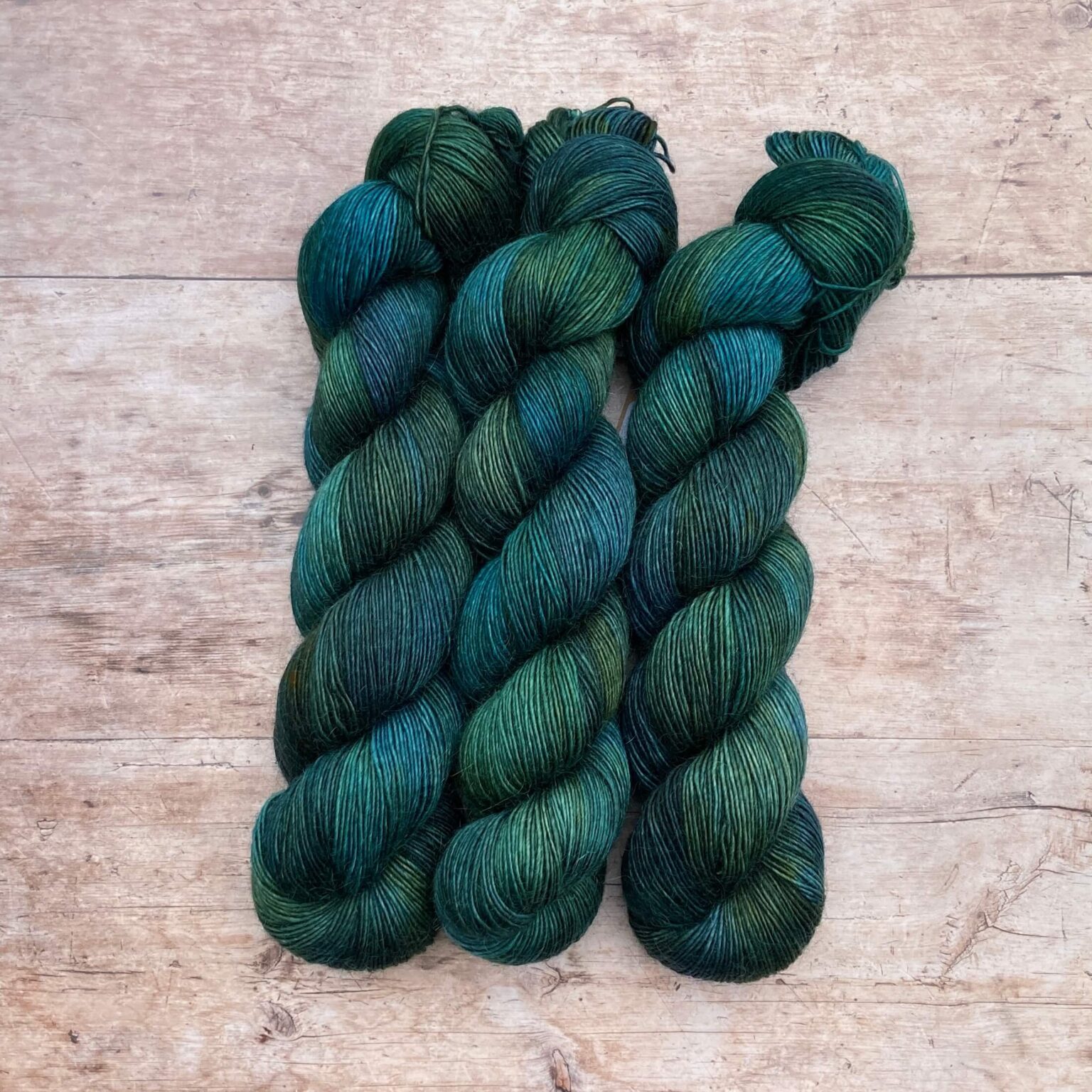 There skeins of Merino Floof in shades of dark blue, green and teal