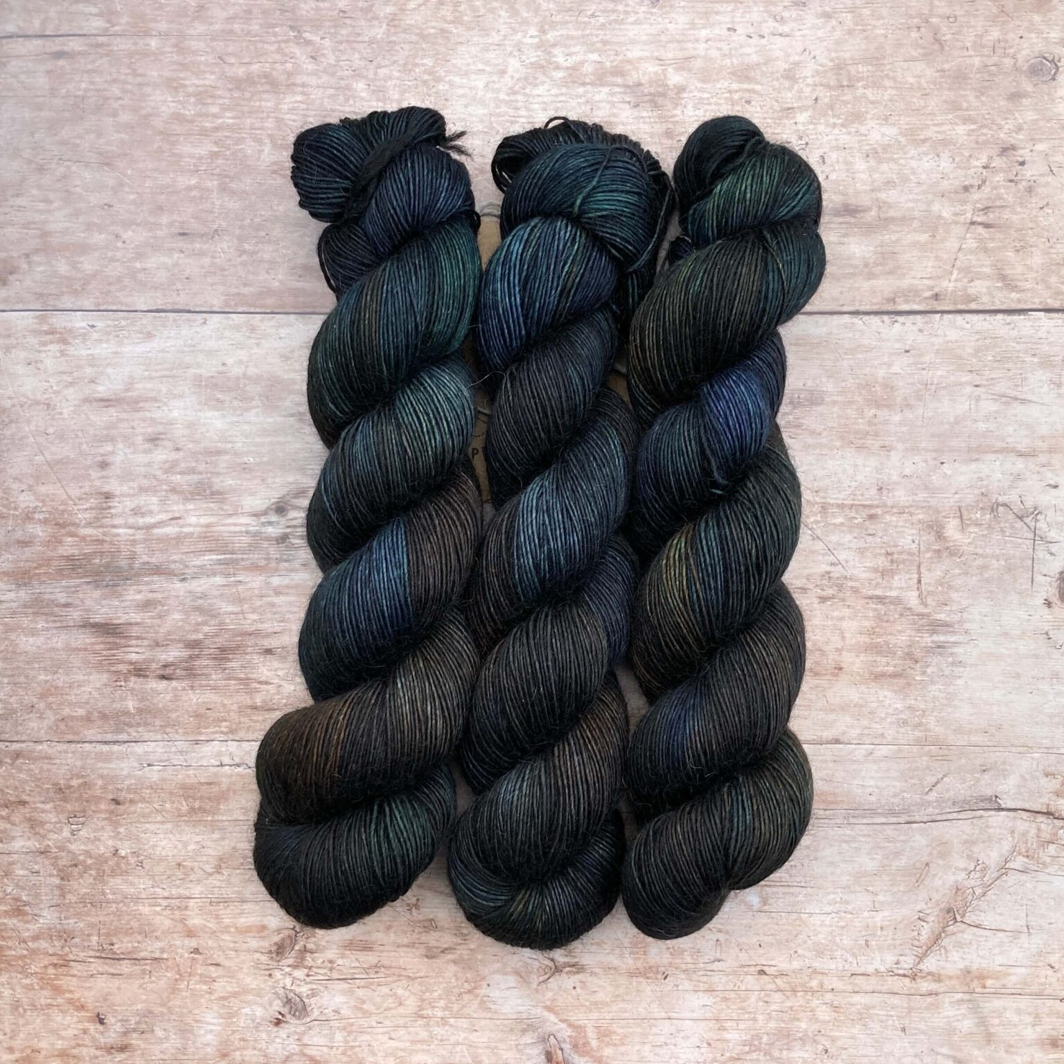 Three skeins of Merino Floof in deep greens, inky blues and rust