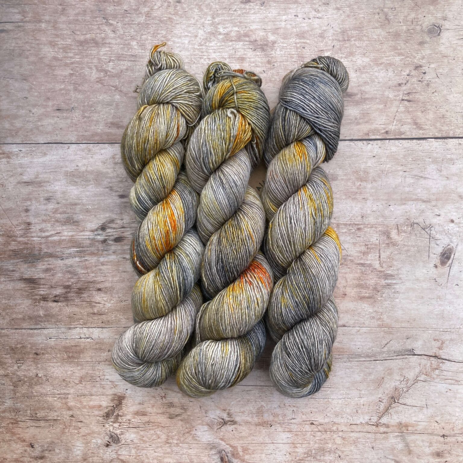 Three skeins of Feather in grey, cream, yellow and orange speckled silky yarn