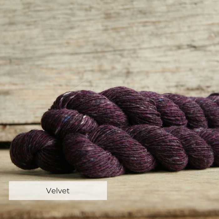 Three skeins of purple tweedy yarn with naps of pink, blue and grey