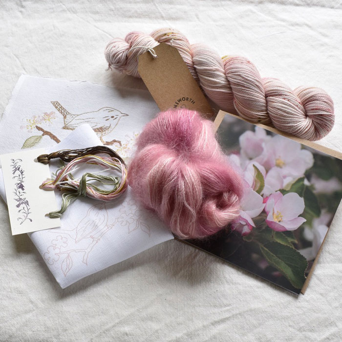 The contents of the club box a skein of pale pink yarn with a mini skein of coordinating pink fluff. There's also an embroidery kit and a card with a photo of the apple blossom