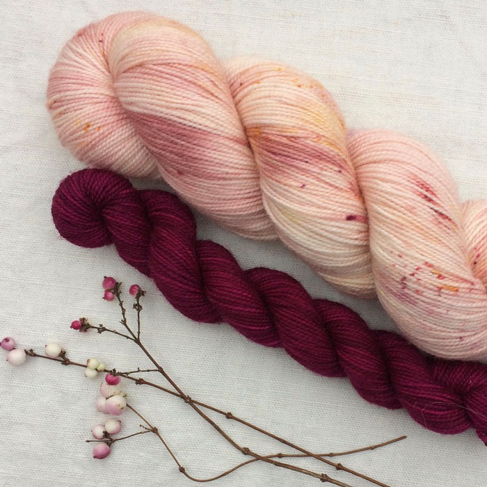 Two skeins of yarn one speckled pink and the other deep dark pink