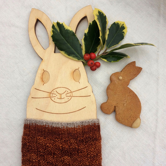 A wooden bunny sock blocker in a ginger sock with a gingerbread rabbit and a sprig of holly