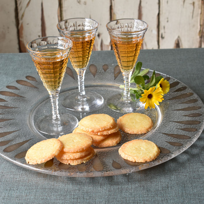 A glass plate with three glasses of sherry and a stack of small cheese biscuits