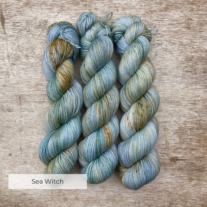 skeins of yarn dyed in shades of pale blue, green and grey with speckles of gold and deep green