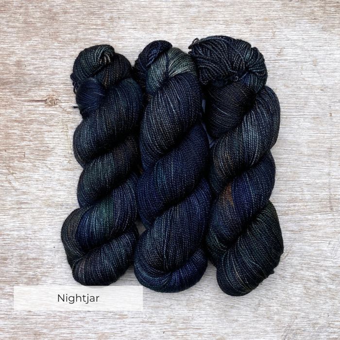 Three skeins of inky blue yarn with splashes of bottle green and rust
