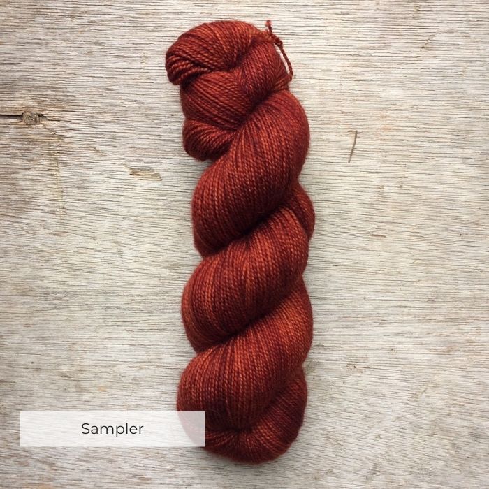 A single skein of orange red sock yarn on a wooden background