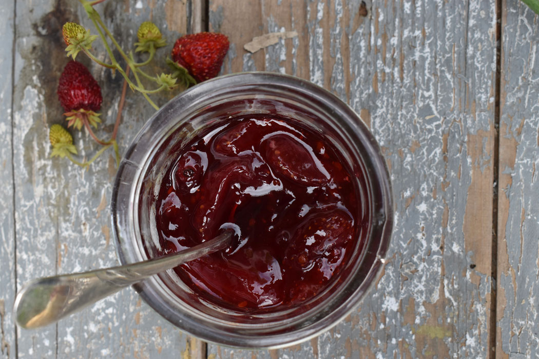 An open jar of homemade jam with a silver teaspoon on the edge of the jar