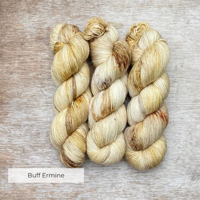 Three plump skeins of creamy yellow yarn with splashes of brown and tan