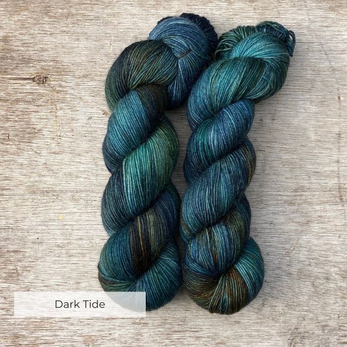 Two skeins of yarn dyed with splashes of navy, emerald and gold