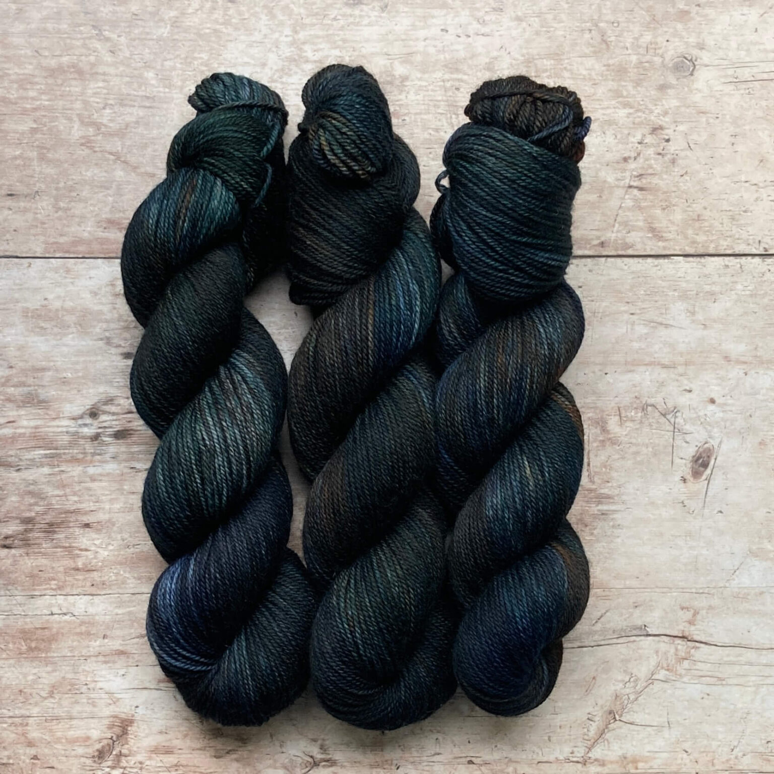 Three skeins of Plump DK in dark blue/green with splashes of brown and rust