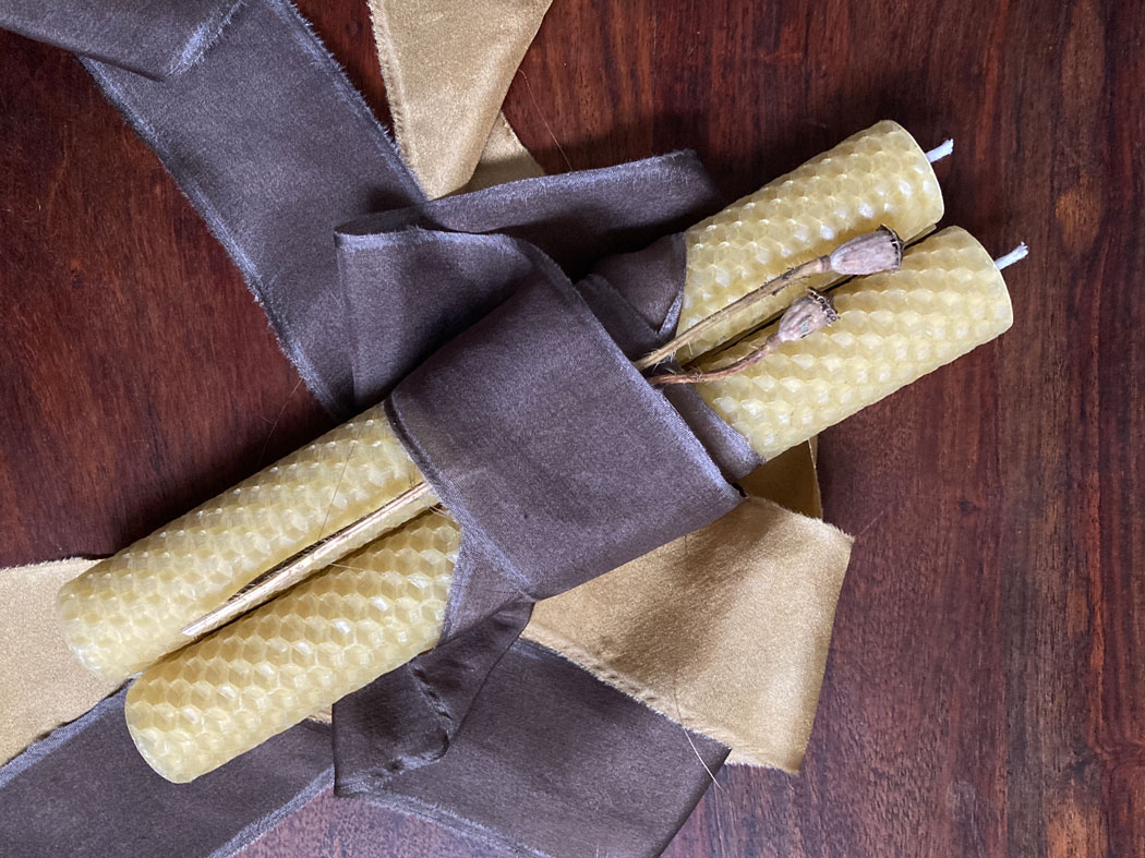 Two beeswax candles wrapped in hand dyed silk ribbon on a wooden table top