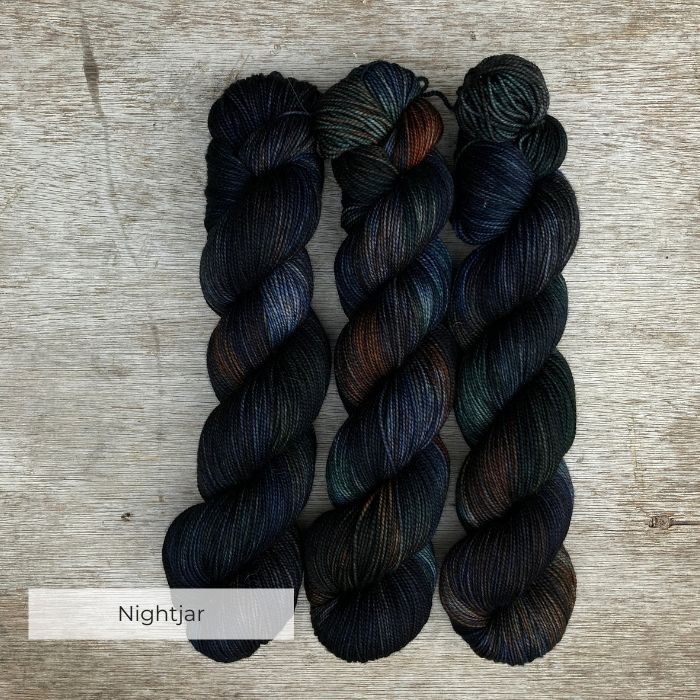 Three skeins of inky blue yarn with splashes of bottle green and rust