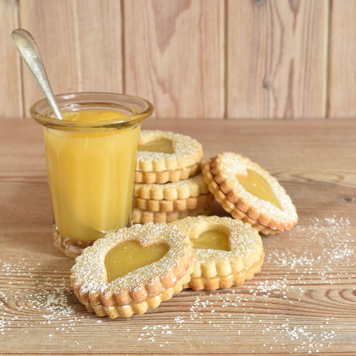 A tottering pile of lemon curd biscuits leaning against a jar of lemon curd