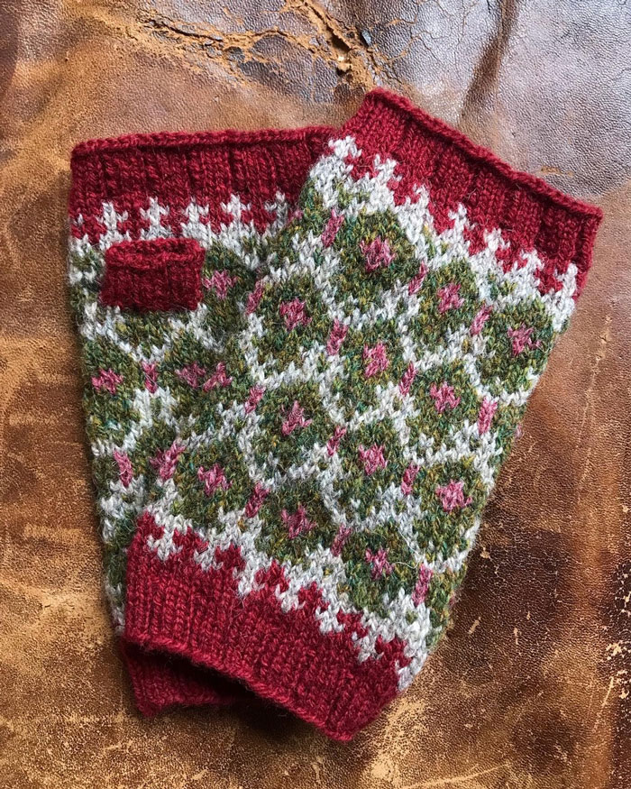 A pair of red fingerless fair isle mittens laying on a battered leather suitcase