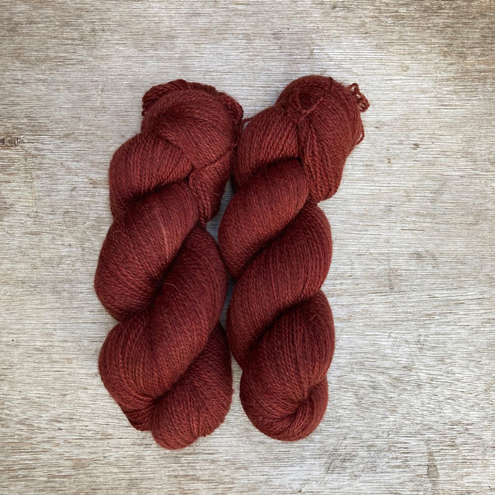 Two skeins of wool on a wood background. The yarn is the colour of faded red oxide