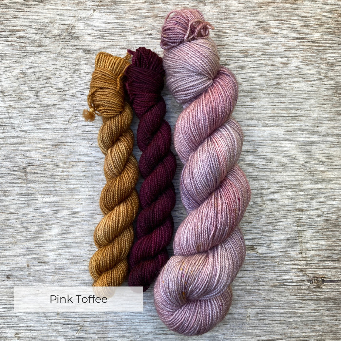 A curving skein of pink speckled yarn with two coordinating minis in toffee and deep red