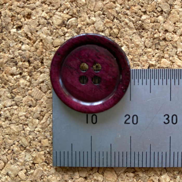A dark pink bone button on a ruler to show the size