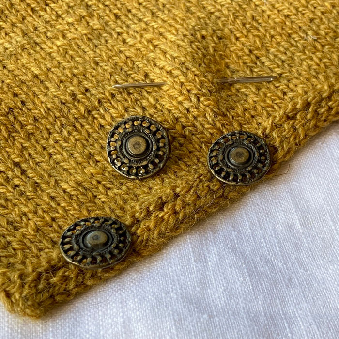 Three metal shank buttons on a piece of knitting