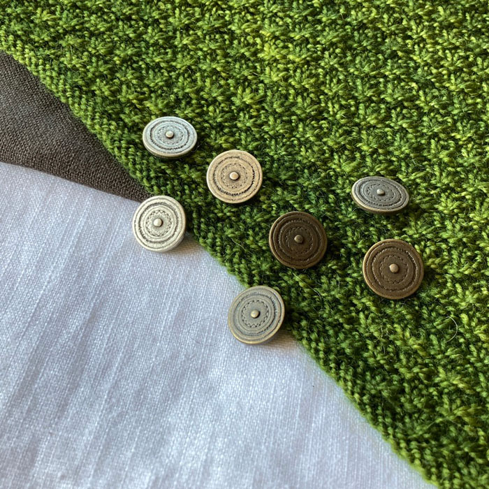 A collection of metal buttons scattered across some knitting