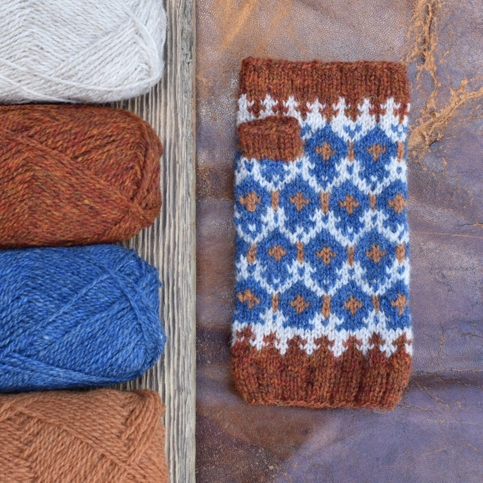 A fairisle mitten laying on a cracked leather surface with the yarn used to make it