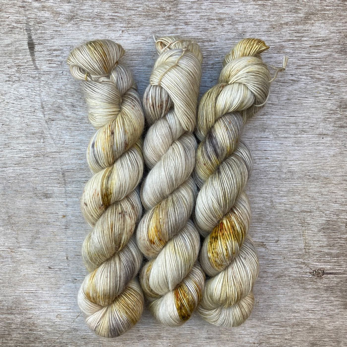 Three skeins of wool in cream, gold and grey