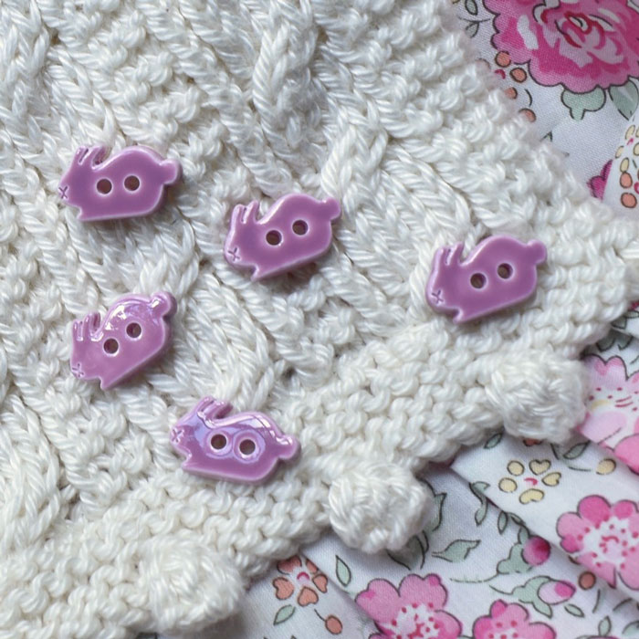 Five pink rabbit buttons on a piece of textured knitting with some floral fabric showing