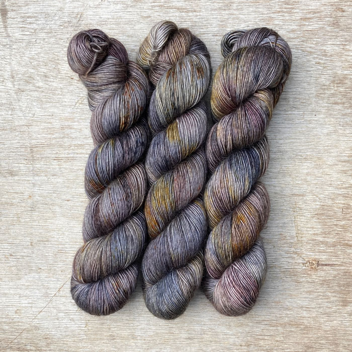 Three multicoloured skeins of wool in dark blues, plum and gold